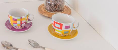 Two colorful coffee cups on a white table with a spoon and scattered coffee beans.
