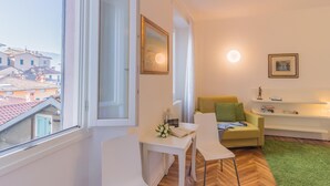 A modern living room with a white sofa, a small table, and a view of the city through a large window. - La Casa di Rosa in Varenna (Varenna)