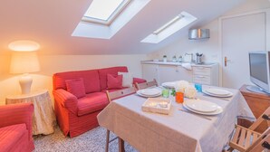 A compact living space with a dining area, a red sofa, a small round table with a lamp, and a kitchenette with a TV. - Varenna Garden in Varenna (Varenna)