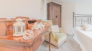 A bedroom with a wooden dresser, a bed, a chair, and a nightstand with decorative items. - Varenna Garden in Varenna (Varenna)