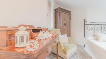 Une chambre à coucher comprenant une commode en bois, un lit, une chaise et une table de chevet agrémentée d’objets décoratifs.