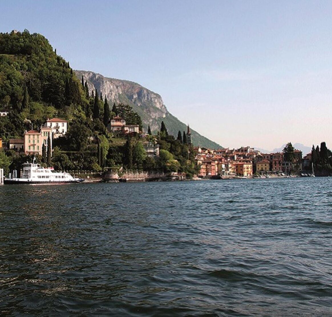 A waterfront town with buildings along the shore, a boat docked near the waterfront, and a mountain in the background.