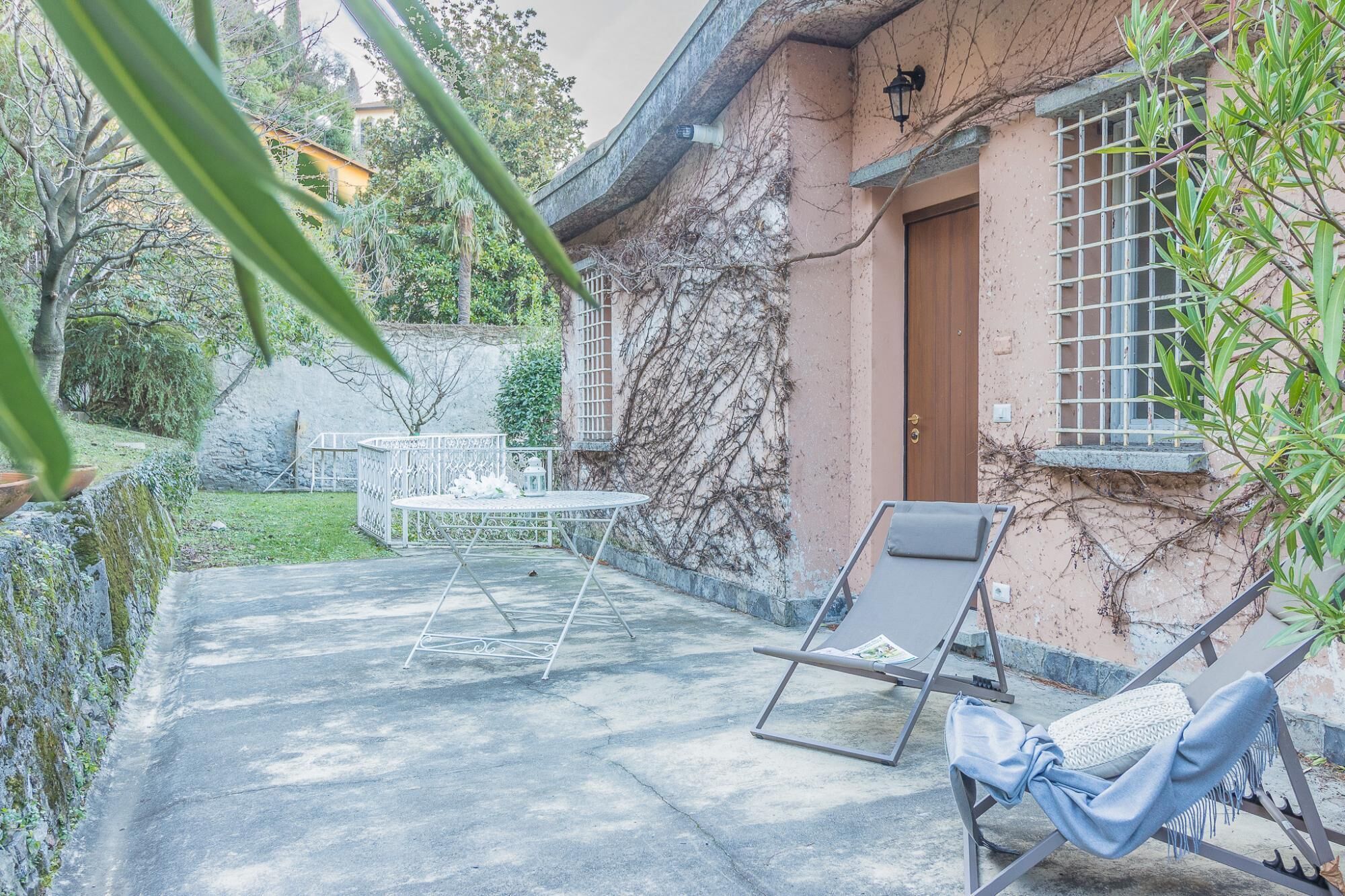A patio with a table and chairs, a lounge chair, and a small garden area with a fence and plants.
