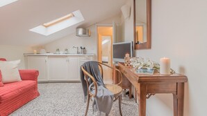 A cozy room with a sloped ceiling, a red sofa, a wooden chair, a wooden table with a mirror, and a kitchen area with a stove and cabinets. - Varenna Garden in Varenna (Varenna)
