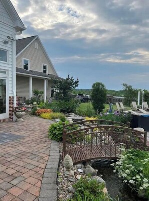 Stroll through the beautifully maintained garden, featuring a variety of plants and flowers, to the traditional house with a front porch.