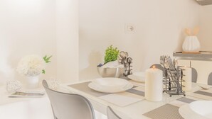 Comedor con una mesa blanca dispuesta para cuatro personas, con platos blancos, un candelabro y una pequeña planta en maceta.