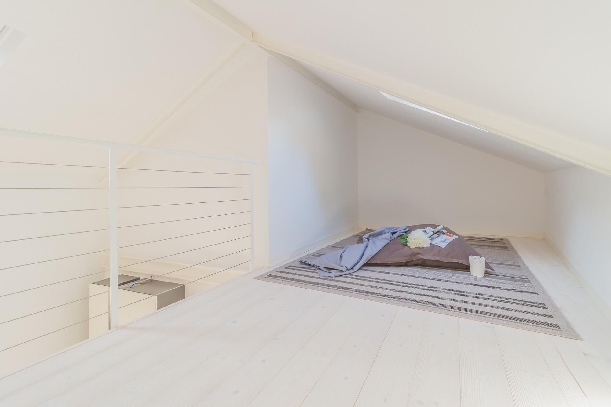 A small attic bedroom with a sloped ceiling, a wooden floor, and a single bed with a blanket and pillow.
