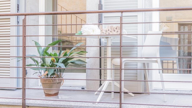 Un balcón con planta en maceta, una silla blanca y una mesa.