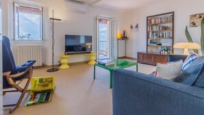 A living room with a sofa, a television, a bookshelf, and a window with a view of mountains. - Casa La Nuvola Varenna (Varenna)