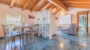 A dining area with a wooden table and chairs, a white shelving unit, and a view of the outdoors through a window. - Casa Del Tiglio in Varenna (Varenna)