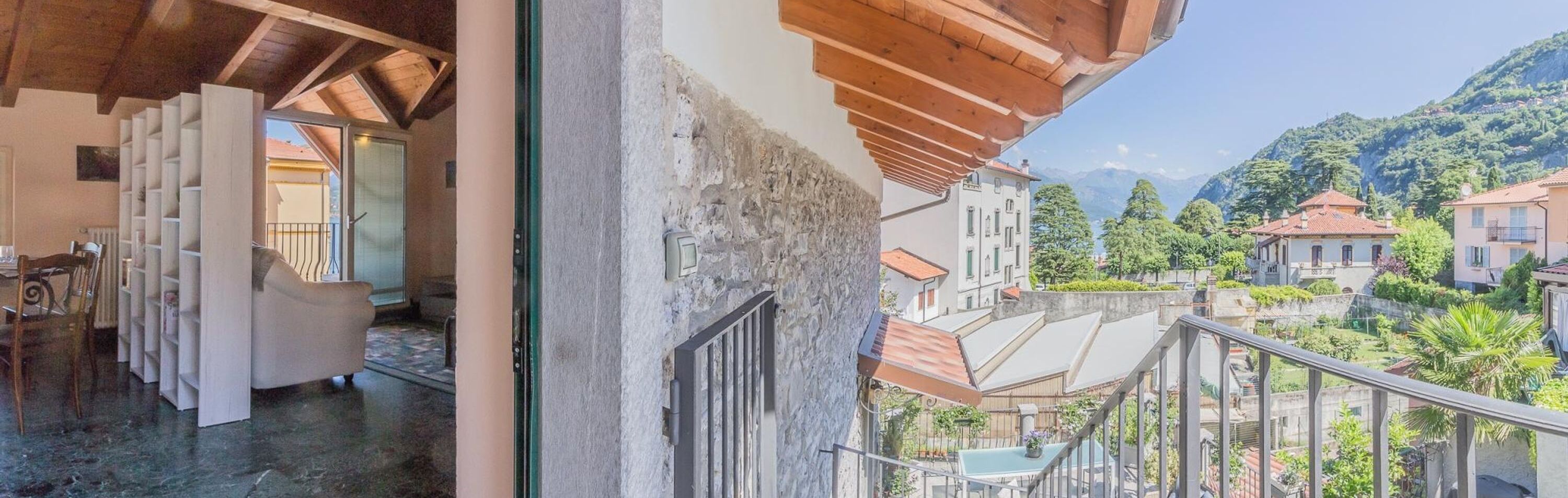 Ein Balkon mit Blick auf eine Hügelstadt, einer Holzbalkendecke und einer Tür zu einem Zimmer mit einem Stuhl und einem Tisch.