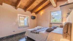 A bedroom with a bed, a window, a TV, and a wooden ceiling. - Casa Del Tiglio in Varenna (Varenna)