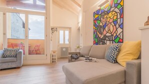 Un salon spacieux avec un grand canapé, un fauteuil plus petit et un tableau abstrait aux couleurs vives accroché au mur.
