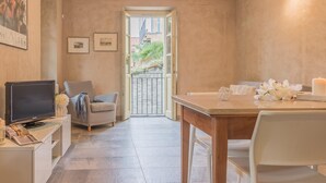 Un salon confortable avec un téléviseur, un canapé, une table à manger avec des chaises et un balcon agrémenté de plantes.