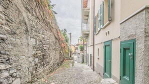 Une ruelle étroite pavée, bordée de murs de pierre et d’immeubles aux portes vertes.