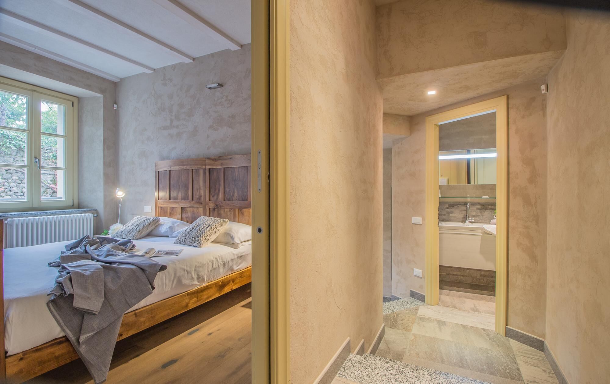 Une chambre à coucher avec un lit en bois, une fenêtre et une salle de bain équipée d’un miroir et d’un lavabo.