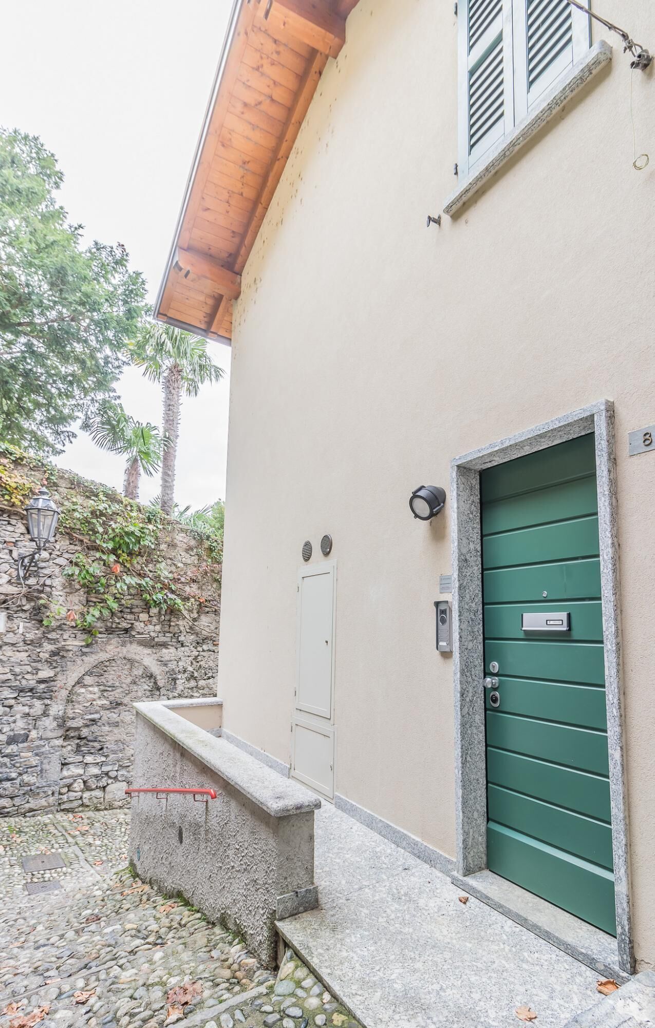 A building with a green door, a stone wall, and a small bench.