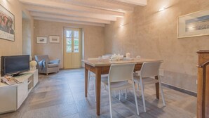 Un coin repas avec une table et des chaises en bois, un téléviseur posé sur un meuble, et une porte donnant sur un balcon.