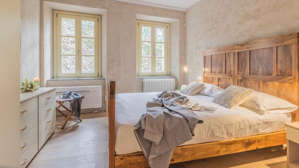 Une chambre à coucher avec un lit en bois, deux fenêtres, un radiateur et une commode en bois.