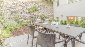 Un patio con pared de piedra, muebles de mimbre y una mesa lista para comer.