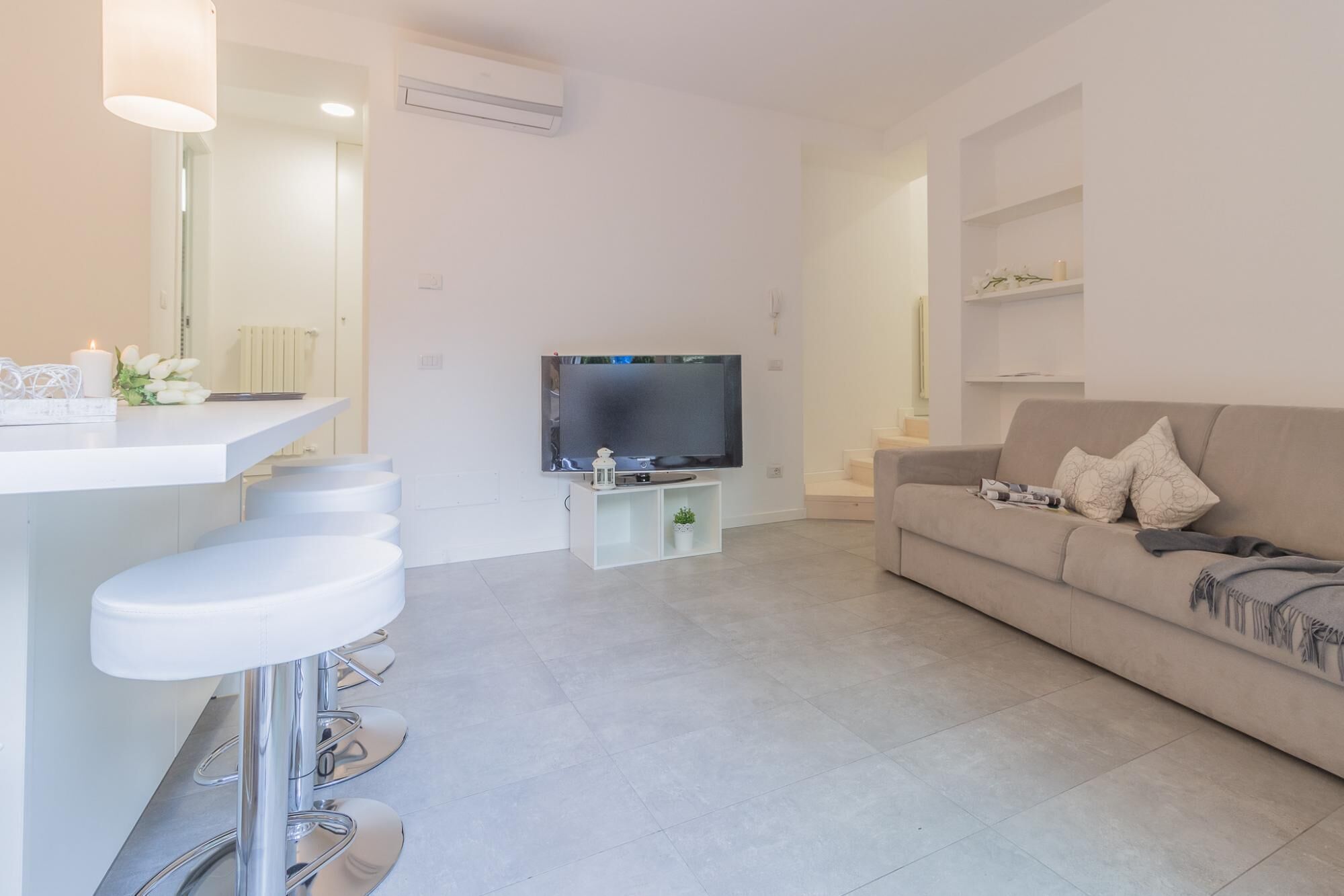 Una sala de estar moderna con un televisor de pantalla plana, un sofá y una barra blanca con taburetes.