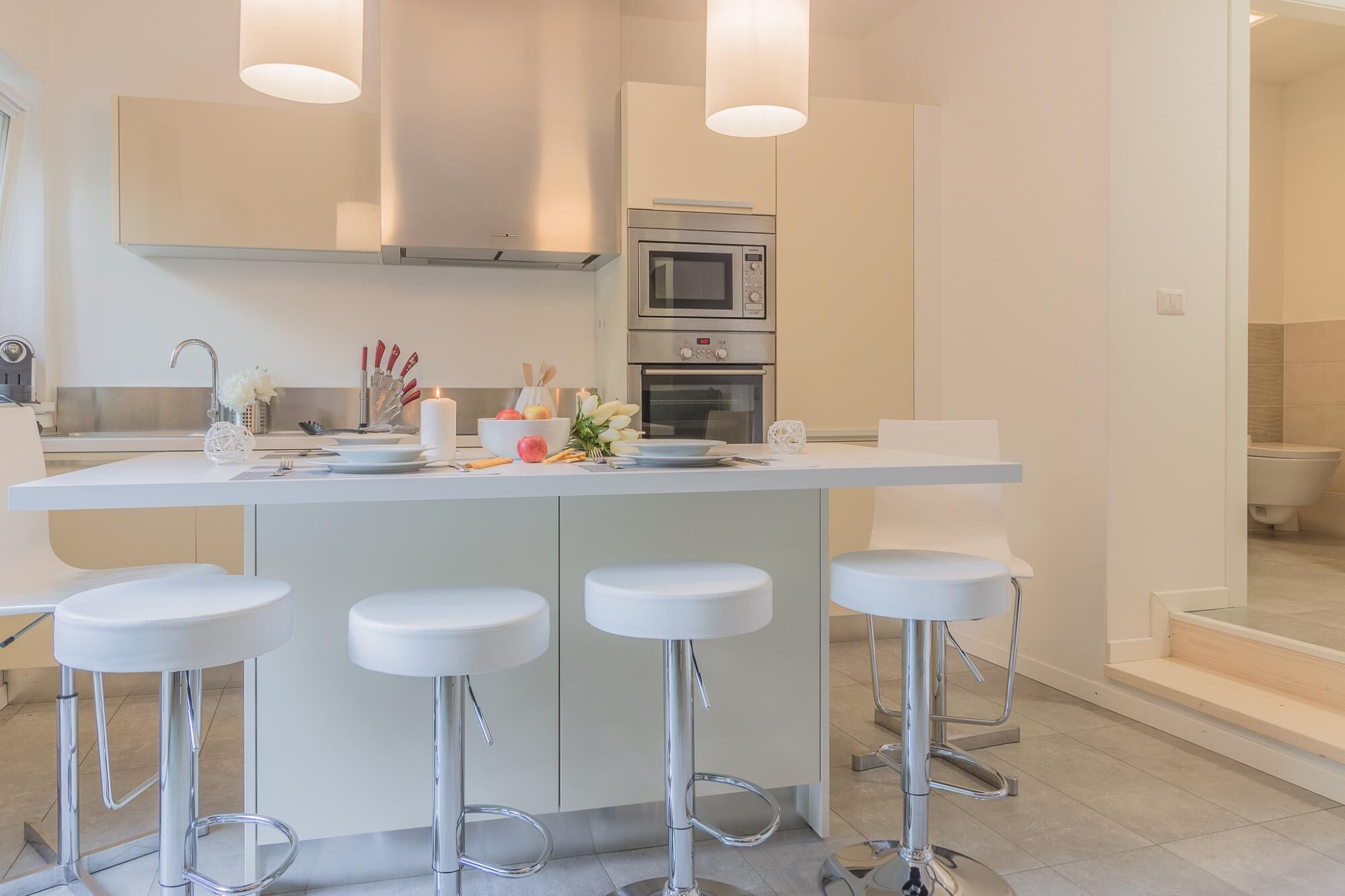 A modern kitchen with a central island, bar stools, a built-in oven, and pendant lighting.