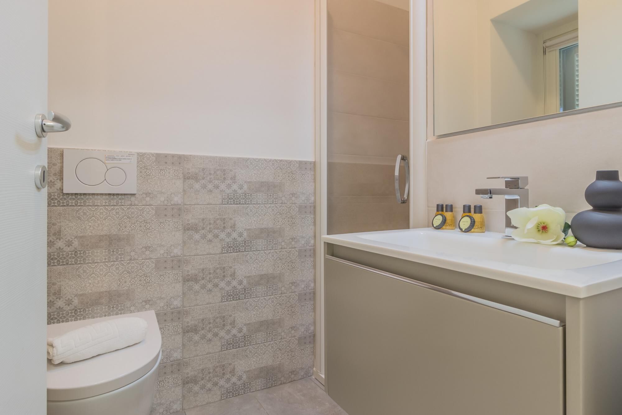 Ein Badezimmer mit Toilette, Dusche und Waschbecken. Auf dem Waschbecken liegen Pflegeprodukte und auf der Toilette ein Handtuch.