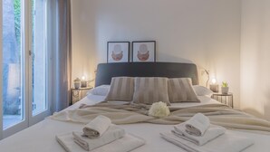 Una habitación de hotel moderna con una cama grande, dos mesitas de noche, un ventanal con cortinas y una obra de arte en la pared.
