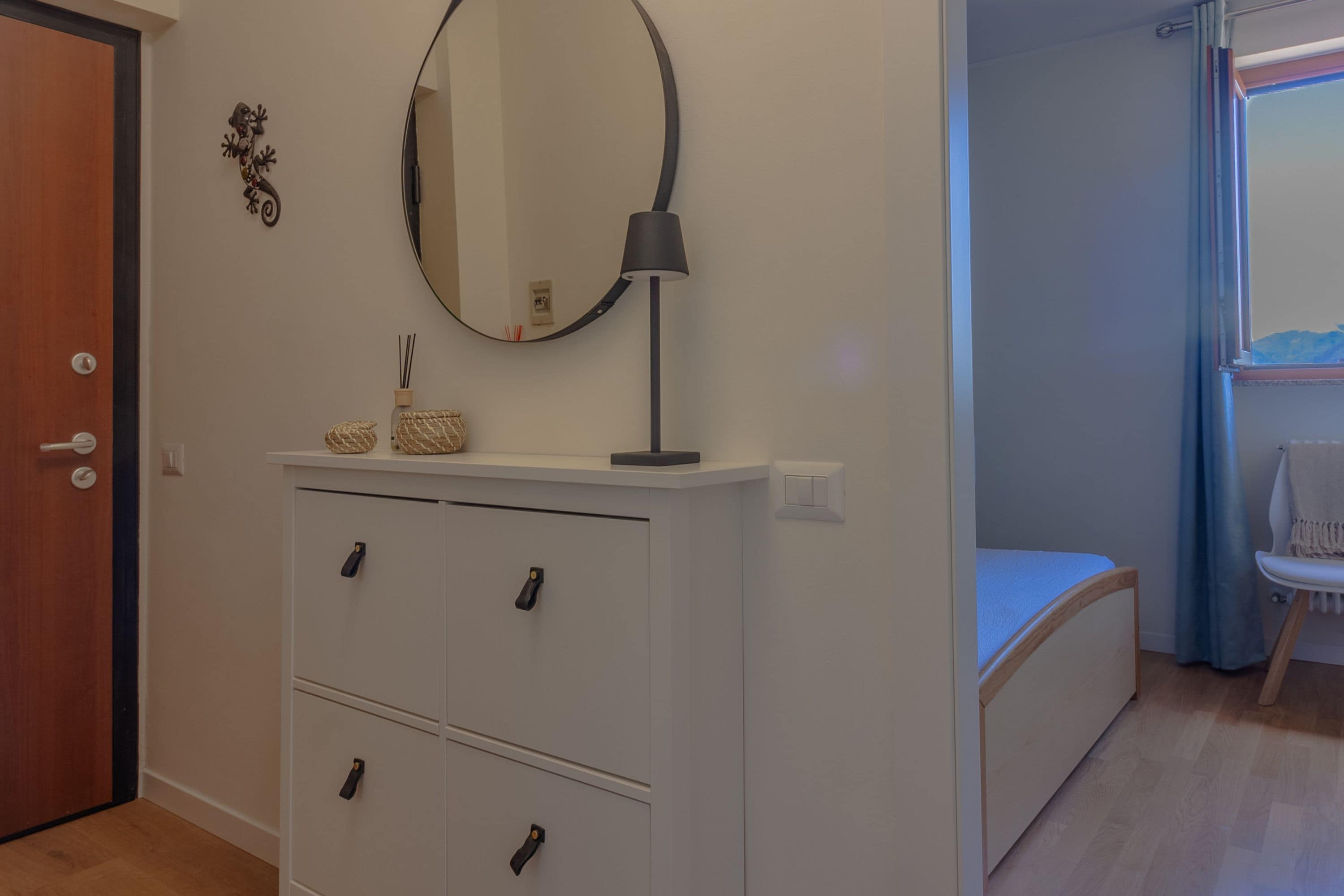 Ein Zimmer mit weißem Schminktisch, einem Spiegel, einer Lampe und einem Bett.
