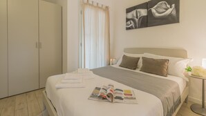 Ein ordentlich bezogenes Bett mit einer Zeitschrift, ein Nachttisch mit einer Vase und ein Bild an der Wand.