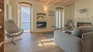 Un salon avec un canapé, un téléviseur, une cheminée et un balcon offrant une vue sur les montagnes.