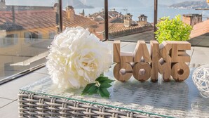 A balcony with a view of a lake and mountains, a white flower, and wooden letters spelling "LAKE COMO". - La Terrazza di Marta (Varenna)