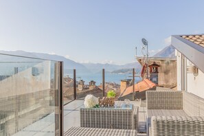 Een balkon met rieten meubilair, een glazen omheining en uitzicht op zee en bergen.