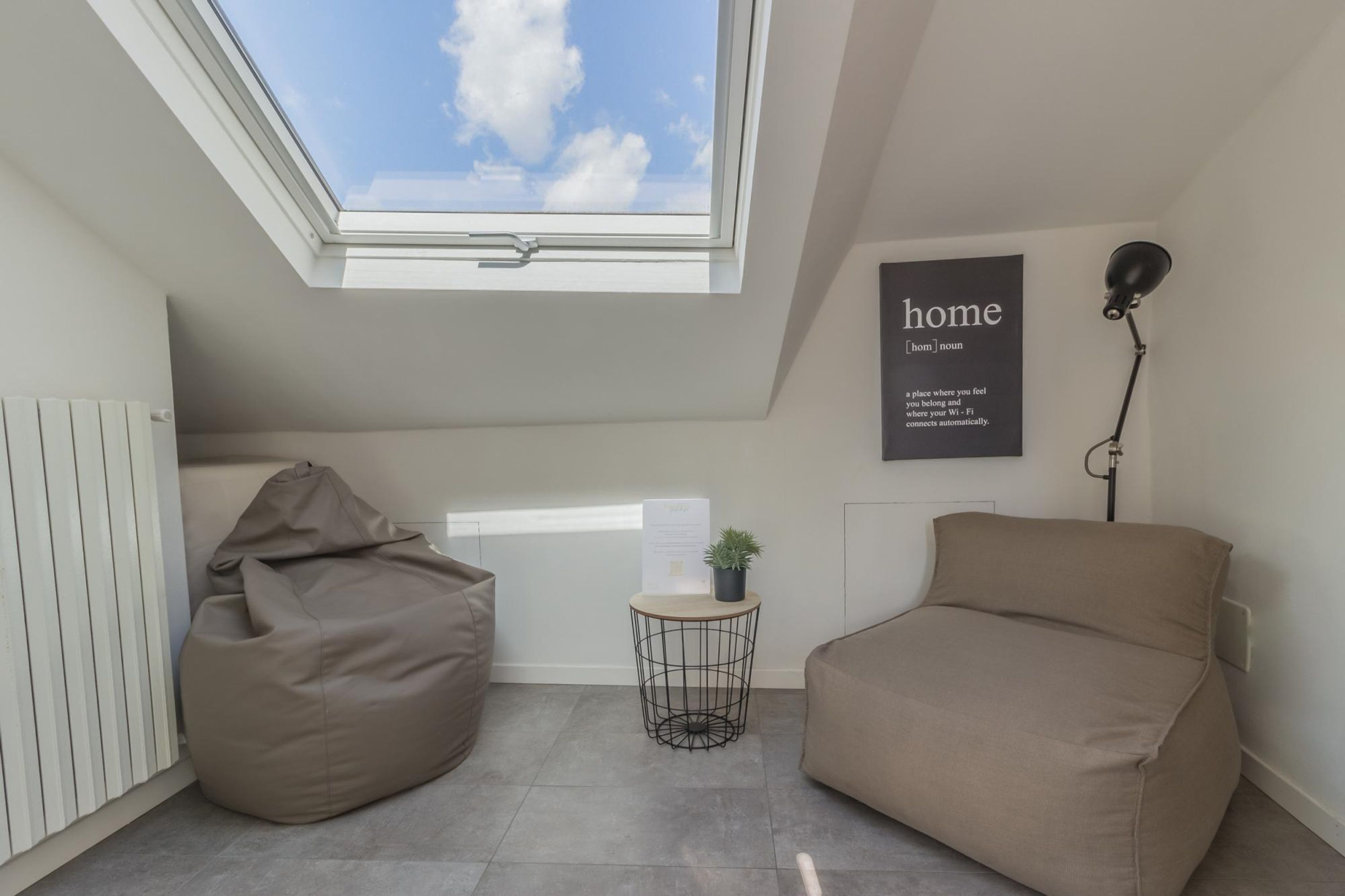 Une chambre moderne avec une lucarne, un fauteuil poire, une petite table avec une plante et un canapé.