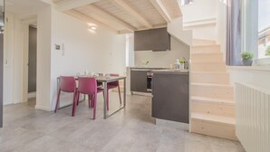 A modern kitchen with a dining area, featuring a staircase, wooden beams, and a view of the outside. - La Terrazza di Marta (Varenna)