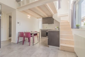 A modern kitchen with a dining area, featuring a staircase, wooden beams, and a view of the outside.
