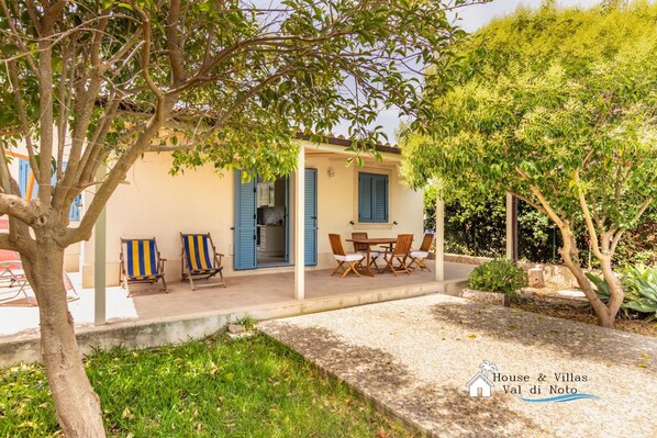 A house with a covered patio, a dining area with a table and chairs, and a small garden.