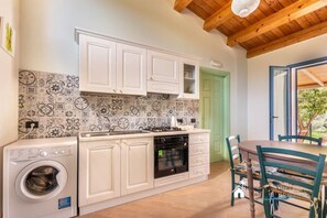 A compact kitchen with white cabinets, a washing machine, and a dining area with a table and chairs.