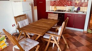 Eine kleine Küche mit einem Holztisch und Stühlen, einem weißen Kühlschrank und roten Schränken.