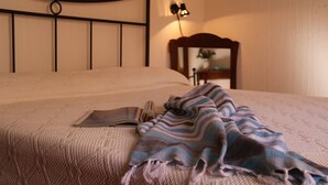 Ein ordentlich bezogenes Bett mit einer gestreiften Decke, einer Nachttischlampe und einem kleinen Tisch mit einer Blumenvase.