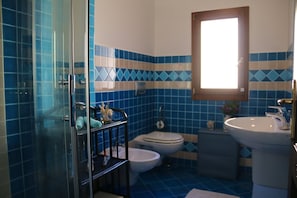 Ein Badezimmer mit blauen Fliesen, einer Glasdusche, einer Toilette, einem Waschbecken und einem Fenster.