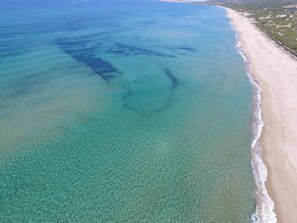 Vista aérea de uma praia com águas turquesa cristalinas e uma extensa faixa de areia.