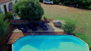 An outdoor swimming pool with a wooden deck, lounge chairs, and a stone wall. - b Giagumeddu 10A Bilo (Badesi)