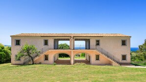 A two-story building with a tiled roof, a central staircase, and a view of the sea. - b Giagumeddu 10A Bilo (Badesi)