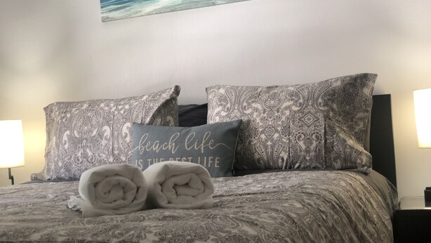A neatly made bed with patterned bedding, two pillows with a beach life quote, and a wall-mounted painting of a beach scene. - *20% OFF Newly Remodeled #3* 5min walk to the Beach, Amazing Virginia Pro Host.  (Norfolk)