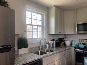 A kitchen with white cabinets, a stainless steel sink, a window, and a microwave.