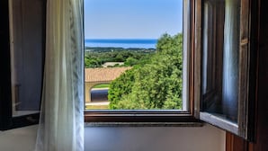 A window with a view of a coastal landscape, including trees and a distant sea. - b Giagumeddu 07A Bilo (Badesi)