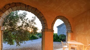 A covered outdoor area with stone arches, a table with chairs, and a view of a garden and building in the background. - d Pietraia 06B Bilo in Badesi (Badesi)