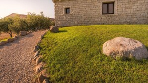 Un edificio de piedra con techo de tejas, un camino de grava y una zona verde con rocas grandes.