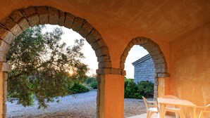 Un patio al aire libre con arcos de piedra, una mesa con sillas y vistas a un jardín y un edificio al fondo.